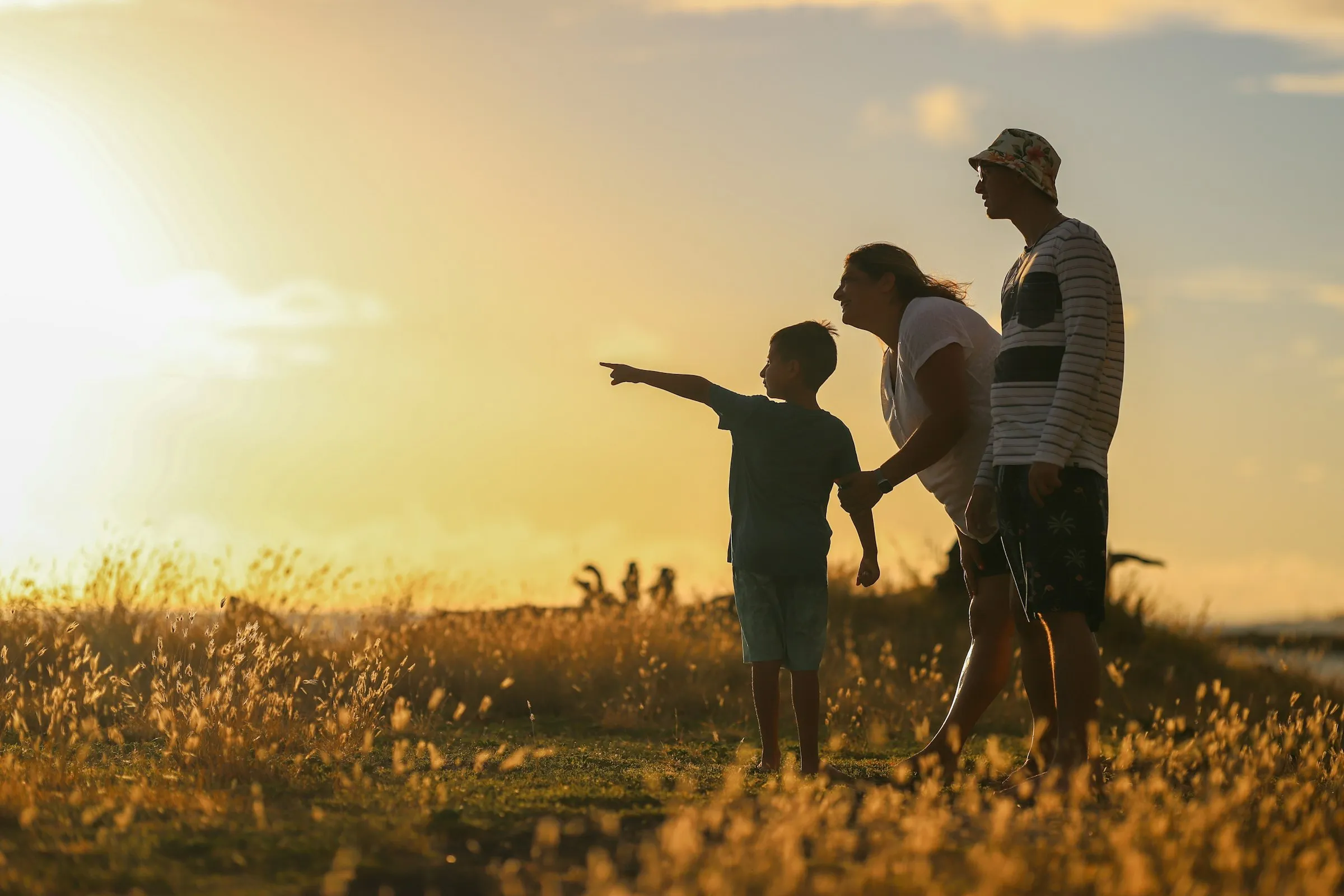 Pai, mãe e filho ao pôr do sol; o menino aponta para o horizonte