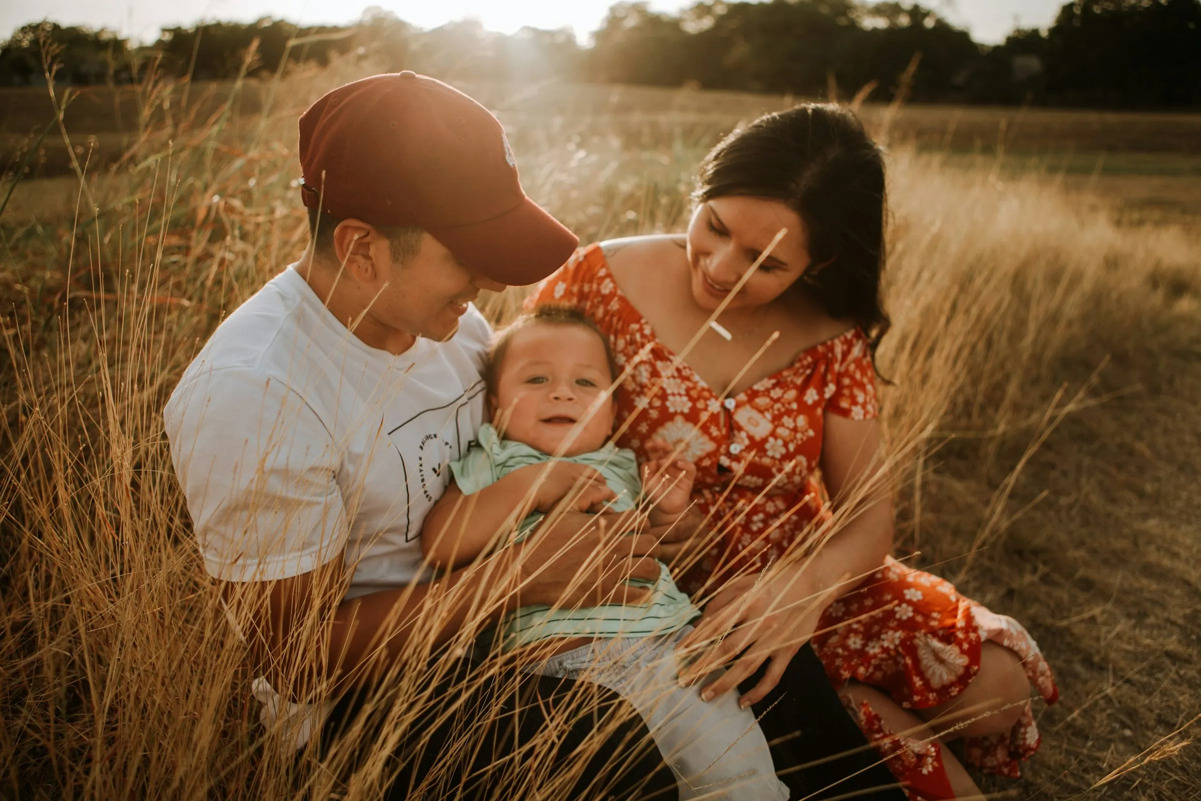 Pai e mãe sentados na erva ao fim da tarde, com o bebé ao colo